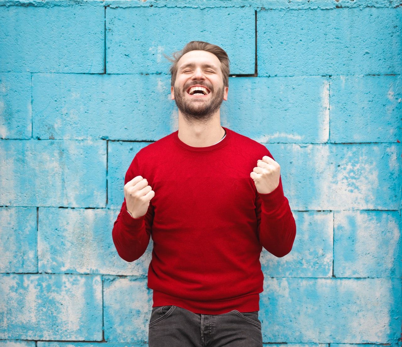 man in red sweater smiling against blue wall