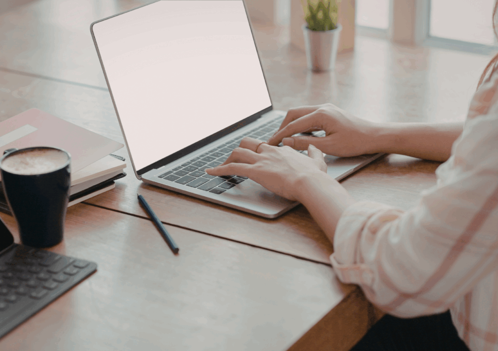 Student typing on a laptop at a wooden desk with a notebook, pen, and coffee, representing the process of writing a personal statement.