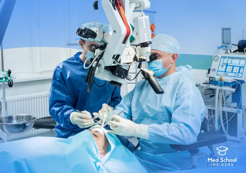 Two neurosurgeons in blue surgical gowns and masks performing a procedure using a surgical microscope on a patient in an operating room.