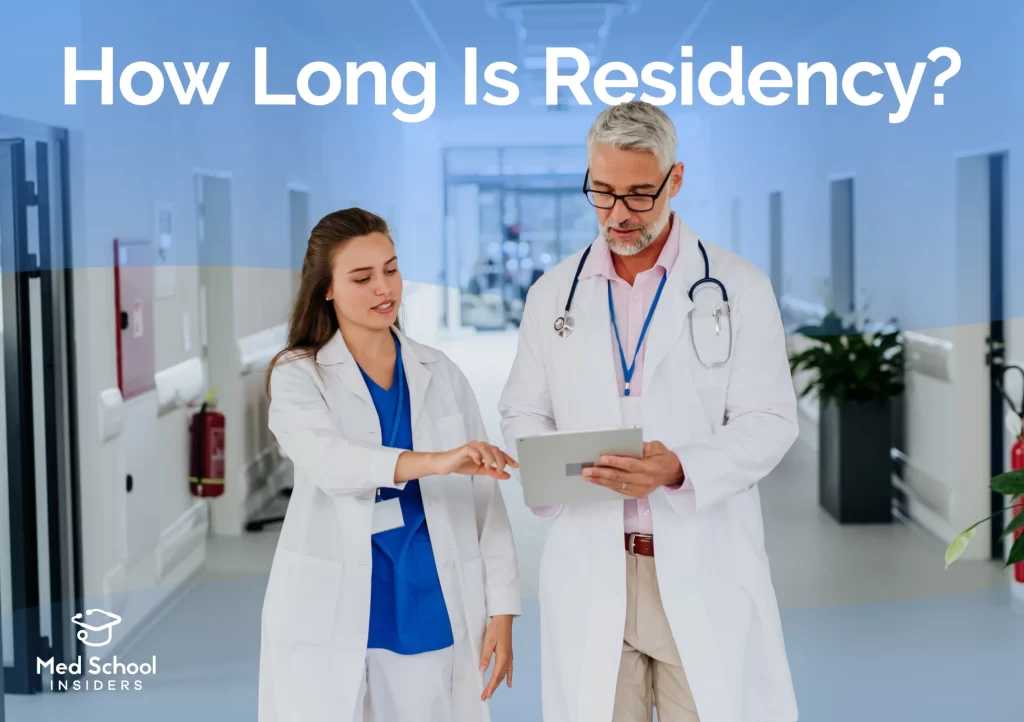 A medical resident and attending physician reviewing a tablet together while walking through a hospital hallway.