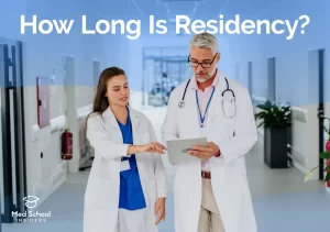 A medical resident and attending physician reviewing a tablet together while walking through a hospital hallway.